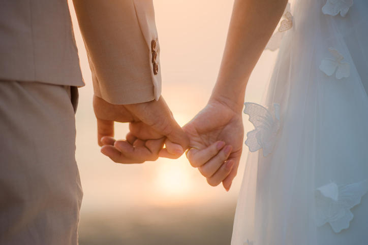 夕日を背景に新郎新婦が小指をつないでいる様子